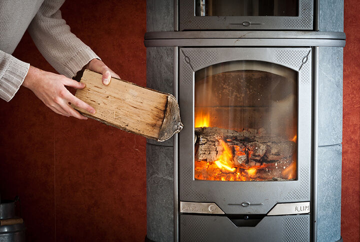 Hand hält Holzscheit vor Kaminofen