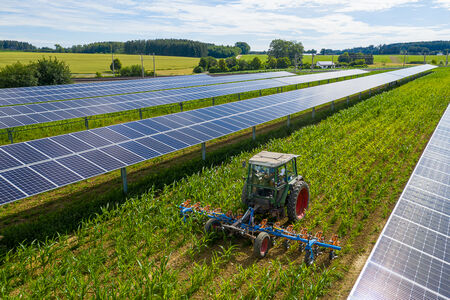 Traktor bei Feldarbeit zwischen Photovoltaik Modulen