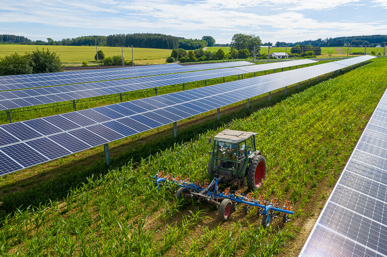 Bild eines Traktors, der ein bestelltes Feld zwischen Photovoltaik-Anlagen pflügt