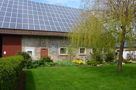 Altes Landhaus mit PV-Modulen auf dem Dach, vorne Rasen