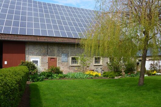 Altes Landhaus mit PV-Modulen auf dem Dach, vorne Rasen